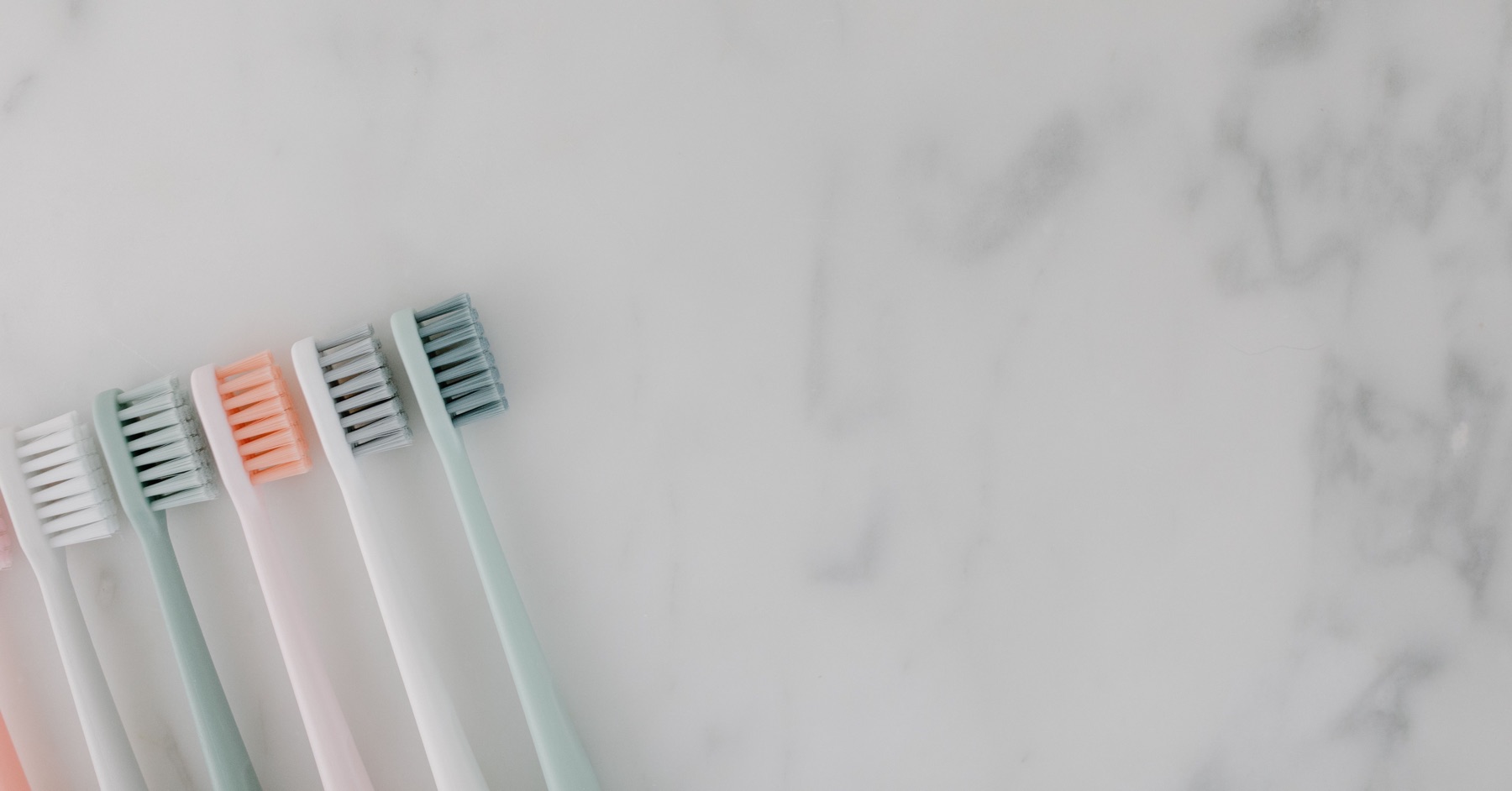 Spazzolini da denti dai colori pastello su un piano chiaro, foto illustrativa