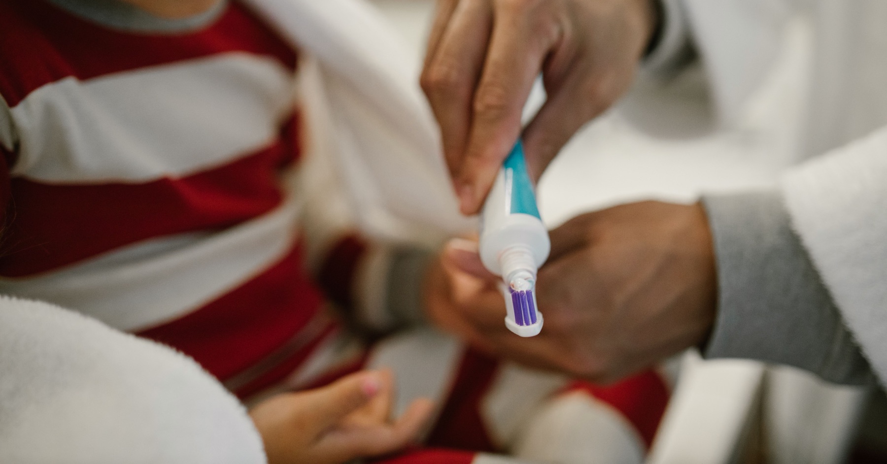 Un adulto mette il dentifricio sullo spazzolino di un bambino, foto illustrativa